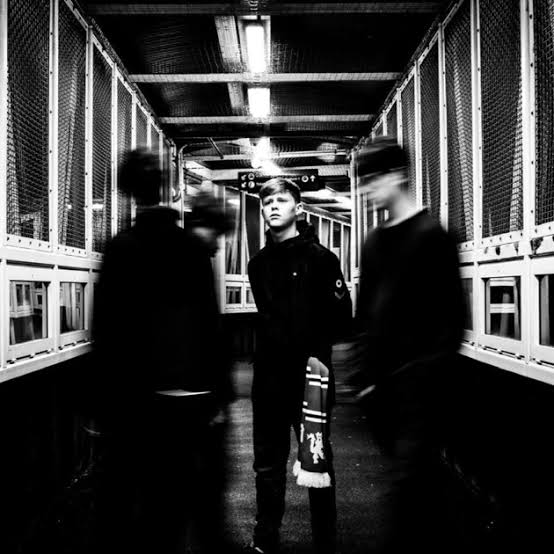 The Fleecers photographed in a Manchester footbridge walkway, motion-blurred bandmates either side